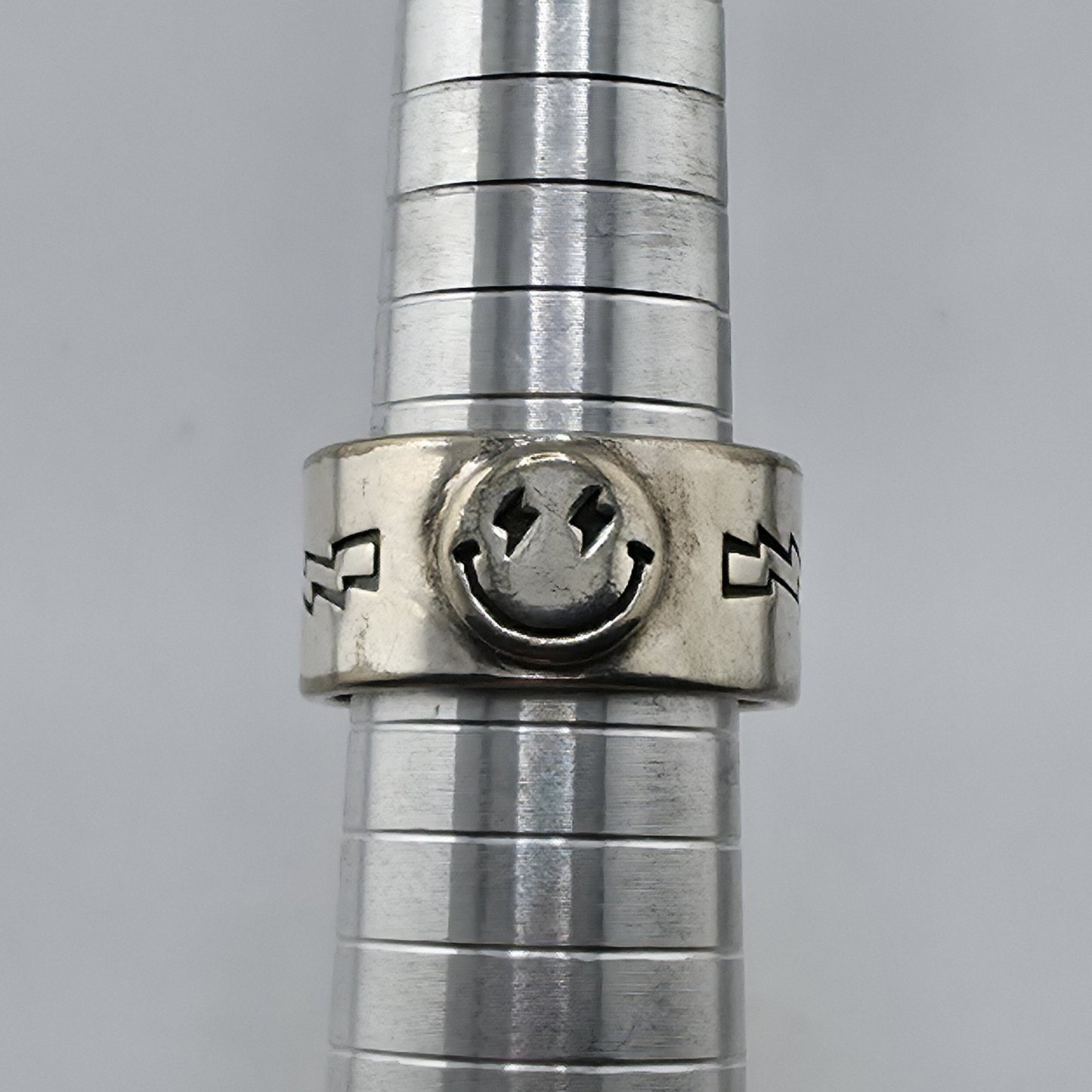 Metallic cylindrical object with a smiley face design on a gray background