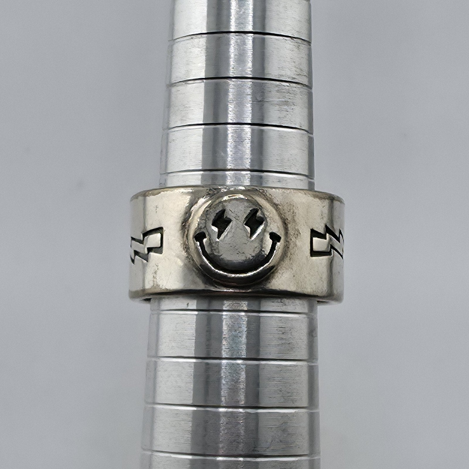 Metallic cylindrical object with a smiley face design on a gray background